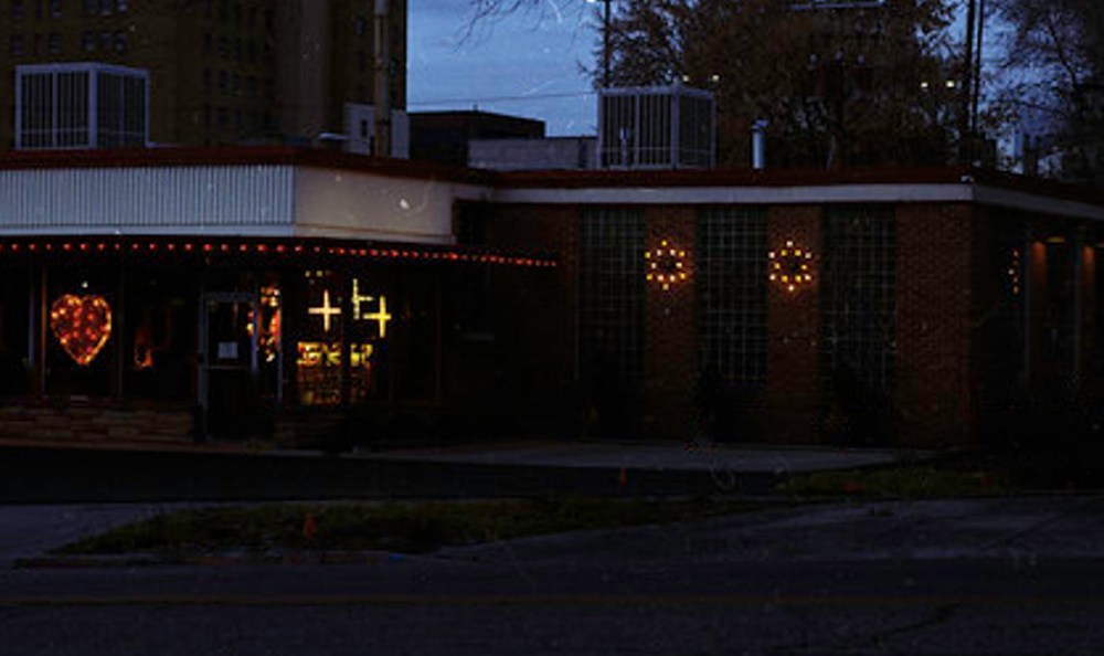 A building at dusk adorned with decorative lights in the shape of a heart and crosses, illuminated windows, and a warm inviting atmosphere.