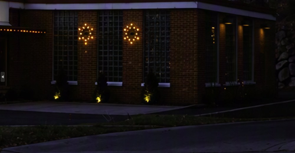 Decorated brick building exterior at night featuring illuminated circular designs on windows and soft lighting along the pathway.