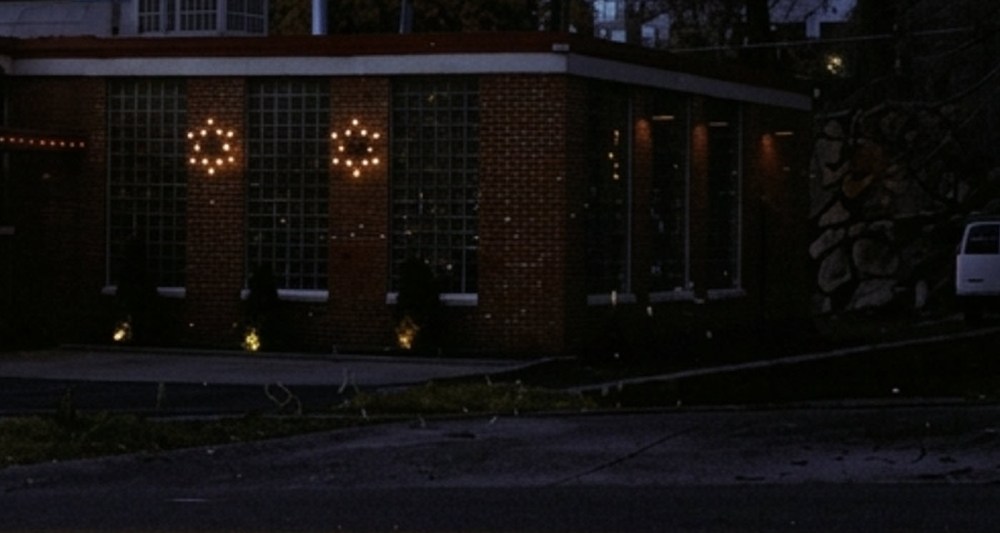 A brick building at night with illuminated glass block windows featuring star-like light decorations, surrounded by dim landscaping.