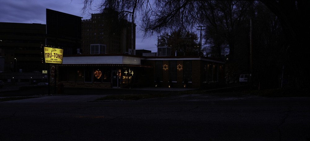 Nighttime view of the Tru-Tone restaurant, featuring a bright yellow sign and illuminated decorations, set against a dark urban backdrop.